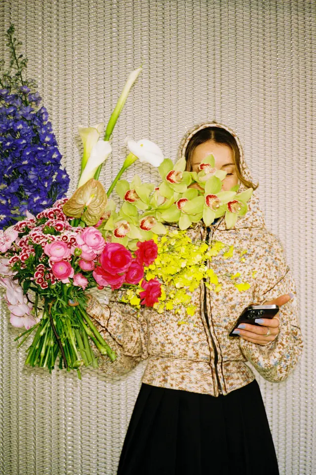 A woman holding an armful of colourful flowers in front of her face