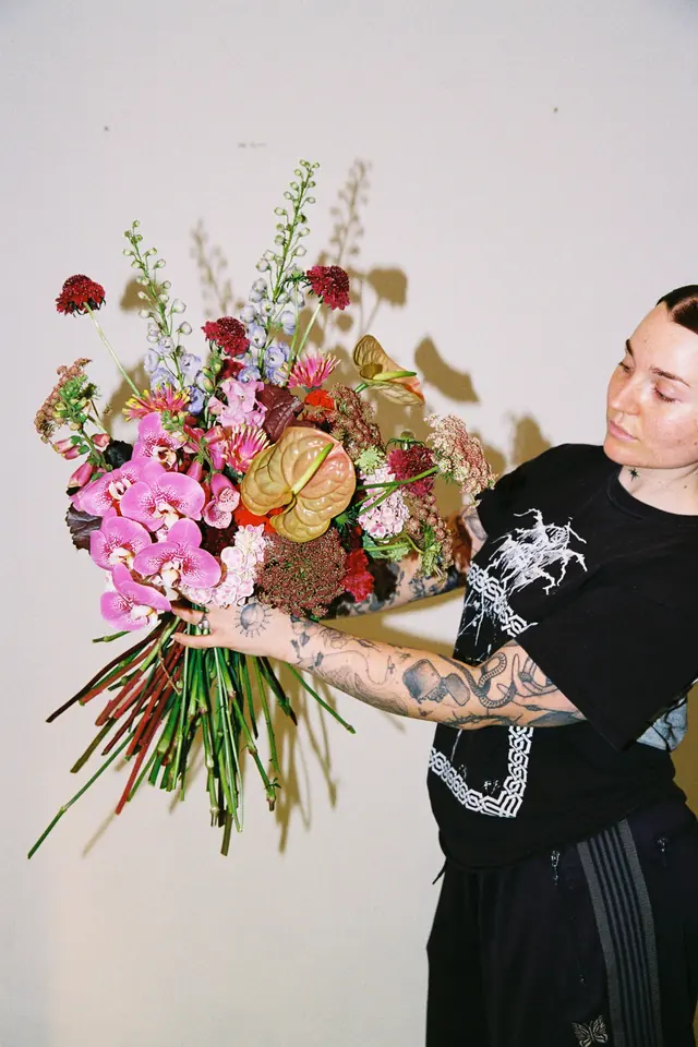 A florist in the XFLOS studio holding a large bouquet of pink orchids, anthurium and delphinium