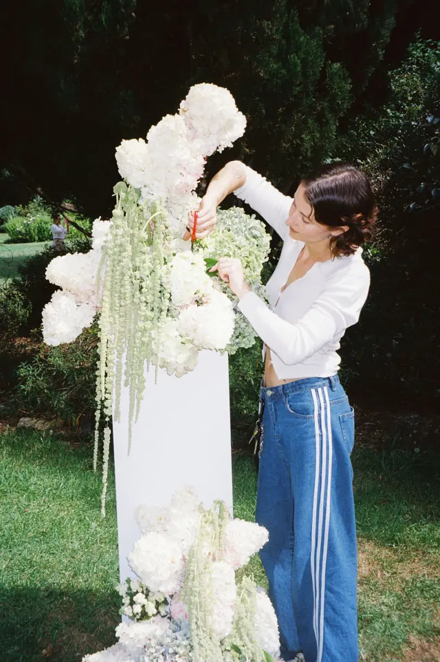 A florist building a white floral installation outdoors