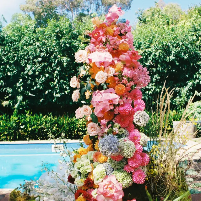 A towering pink, coral and orange floral installation beside a pool
